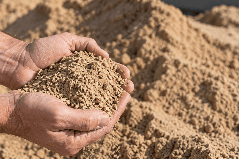 Kiepwagen van Zandbezorgen lost zand op een oprit